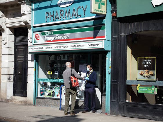 Day Two of Lockdown in Peterborough. A person from a pharmacy speaks to a customer outside of the shop in Peterborough. The country is on lockdown due to the COVID-19 Coronavirus pandemic. People are not allowed to leave home except for minimal food shopping, medical treatment, exercise - once a day, and essential work. COVID-19 Coronavirus lockdown, Peterborough, Cambridgeshire, UK, on March 25, 2020 