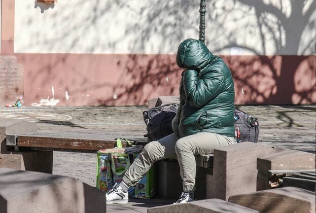 Ein Obdachloser sitzt eingemummt in der waermenden Sonne auf dem menschenleeren Rathausplatz in Freiburg. In Zeiten von Corona verschlechtern sich die Anlaufmoeglichkeiten und Hilfsangebote für Obdachlose dramatisch. Waermestuben, Tafeln etwa haben geschlossen. Foto:Winfried Rothermel