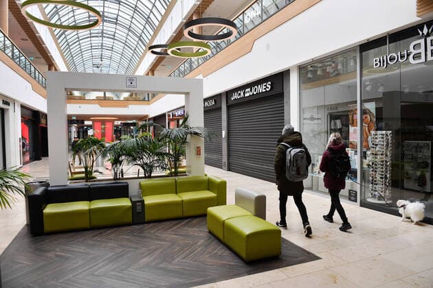 Leere Gaenge und Rolltreppen-geschlossene Laeden,Geschaefte,Shops. Zwei Passanten gehen mit einem Hund an der Leine an geschlossenen Shops vorbei. Geschlossenes Einkaufszentrum wegen Corona Pandemie,Shopping Center,Riem Arcaden am 26.03.2020.