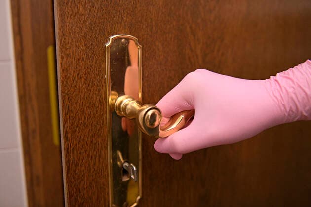 26.03.2020, Frau drückt mit Gummihandschuhen eine Türklinke zum Schutz vor Bakterien und Viren. 26.03.2020, Infektionsschutz 26.03.2020, Infektionsschutz