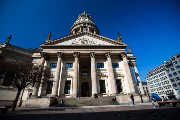 Einige wenige Menschen geniesesen vereinzelt die Sonne am Gendarmenmarkt in Berlin am 26. Maerz 2020. Um die Verbreitung des Coronavirus (SARS-CoV-2) zu verlangsamen beschlossen Bund und Laender weitere Restriktionen. Nachdem Museen, Theatern, Sportveranstaltungen usw verboten wurden sind seit einigen Tagen weitere verschaerfte Massnahmen in Kraft getreten wie z.B. Verbot von Versammlungen in der Oeffentlichkeit mit mehr als zwei Personen, Einhaltung von Mindestabstand zwischen Personen und Schliessung von Gastronomiebetrieben mit Ausnahme vn Abholung und Lieferung. Oeffentliches Leber weiter in Berlin wegen Coronavirus eingeschraenkt