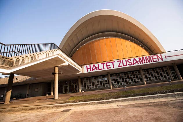 Schrift Haltet Zusammen, mit ein Bisschen Abstand auf dem Haus der Kulturen der Welt in Berlin am 27. Maerz 2020. Um die Verbreitung des Coronavirus (SARS-CoV-2) zu verlangsamen beschlossen Bund und Laender weitere Restriktionen. Nachdem Museen, Theatern, Sportveranstaltungen usw verboten wurden sind seit einigen Tagen weitere verschaerfte Massnahmen in Kraft getreten wie z.B. Verbot von Versammlungen in der Oeffentlichkeit mit mehr als zwei Personen, Einhaltung von Mindestabstand zwischen Personen und Schliessung von Gastronomiebetrieben mit Ausnahme vn Abholung und Lieferung. Oeffentliches Leber weiter in Berlin wegen Coronavirus eingeschraenkt