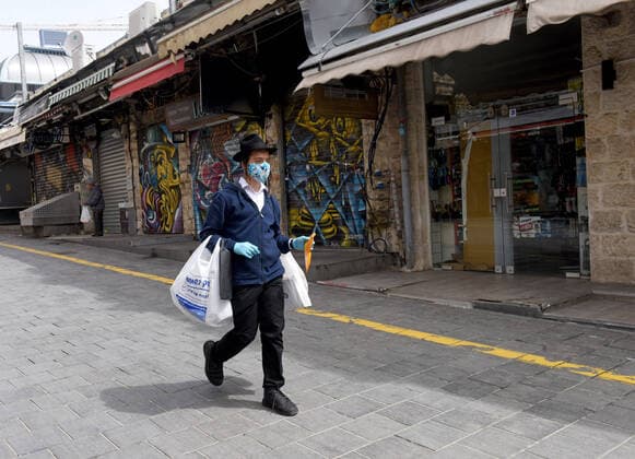 An Ultra-Orthodox Israeli wears protective mask and gloves while walking past closed shops in the Mahane Yehuda Market in Jerusalem, on Friday, March 27, 2020. Eleven Israelis have died from the coronavirus, while more than 3,000 have been diagnosed with the disease. The Israeli government has imposed tight restrictions of movement, leaving only essential stores open in an effort to stop the spread of the coronavirus.  JER2020032702 DEBBIExHILL