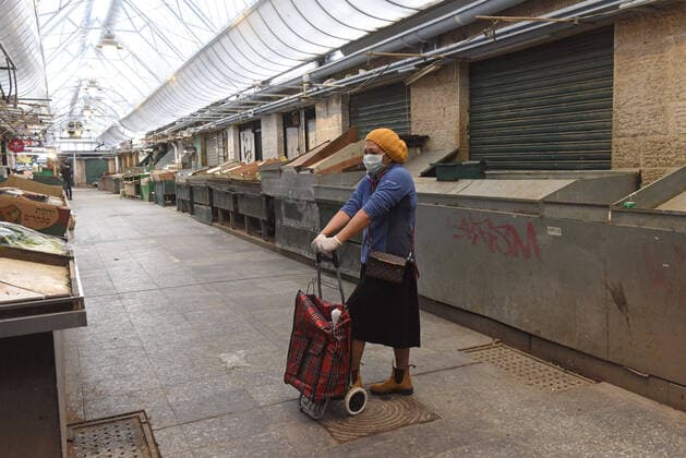 A woman wears protective mask and gloves while standing in the shuttered Mahane Yehuda Market in Jerusalem, on Friday, March 27, 2020. Eleven Israelis have died from the coronavirus, while more than 3,000 have been diagnosed with the disease. The Israeli government has imposed tight restrictions of movement, leaving only essential stores open in an effort to stop the spread of the coronavirus.  JER2020032703 DEBBIExHILL
