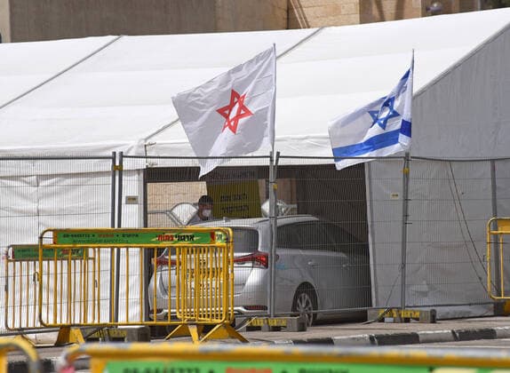A member of Magen David Adom wears protective clothing while working in a coronavirus drive through tent in Jerusalem, on Friday, March 27, 2020. Eleven Israelis have died from the coronavirus, while more than 3,000 have been diagnosed with the disease. The Israeli government has imposed tight restrictions of movement, leaving only essential stores open in an effort to stop the spread of the coronavirus.  JER2020032714 DEBBIExHILL