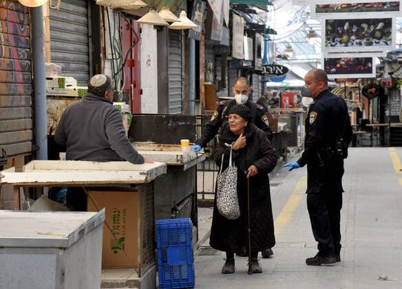 Israeli police wear protective masks and gloves, while warning a vendor to close his shop, in the partically closed Mahane Yehuda Market in Jerusalem, on Friday, March 27, 2020. Eleven Israelis have died from the coronavirus, while more than 3,000 have been diagnosed with the disease. The Israeli government has imposed tight restrictions of movement, leaving only essential stores open in an effort to stop the spread of the coronavirus.  JER2020032707 DEBBIExHILL