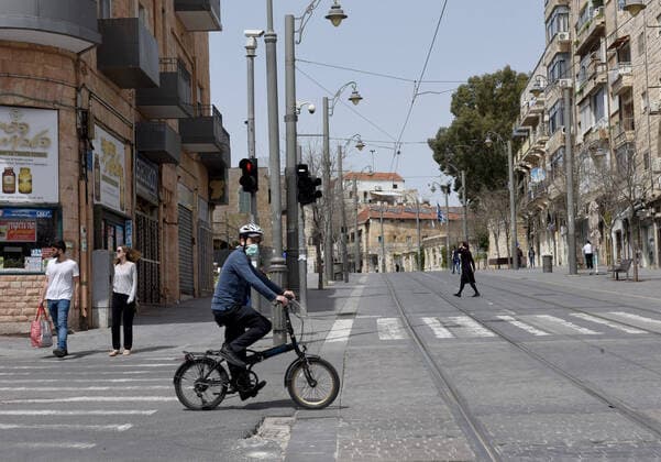 An Israeli wears a protective mask while riding a bike on an empty street in Jerusalem, on Friday, March 27, 2020. Eleven Israelis have died from the coronavirus, while more than 3,000 have been diagnosed with the disease. The Israeli government has imposed tight restrictions of movement, leaving only essential stores open in an effort to stop the spread of the coronavirus.  JER2020032719 DEBBIExHILL