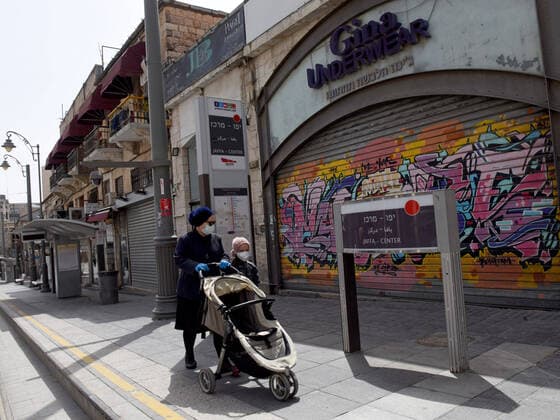 Israelis wear protective masks and gloves while walking on an empty sidewalk in Jerusalem, on Friday, March 27, 2020. Eleven Israelis have died from the coronavirus, while more than 3,000 have been diagnosed with the disease. The Israeli government has imposed tight restrictions of movement, leaving only essential stores open in an effort to stop the spread of the coronavirus.  JER2020032720 DEBBIExHILL