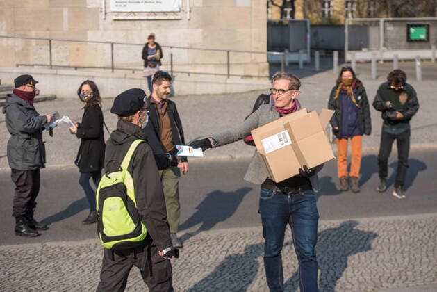 Trotz Ausgangsbeschraenkungen haben am Samstag (28.03.2020) auf dem Rosa-Luxemburg-Platz vor der Berliner Volksbuehne etwa 80 Menschen an einer Hygienedemo fuer Verfassung, Grundrechte & transparente Gestaltung der neuen Wirtschaftsregeln durch die Menschen selbst teilgenommen. (Foto: Ein Demonstrant verteilt Exemplare des Grundgesetz) Jeweils mit dem Grundgesetz unter dem Arm forderten die Demonstranten im Kreis laufend unter anderem die Beendigung des Notstands-Regimes , demokratische Regeln fuer unser kuenftiges Wirtschaftssystem und die Verhinderung obrigkeitsstaatlicher Schikanen . (Siehe epd-Meldung vom 28.03.2020)