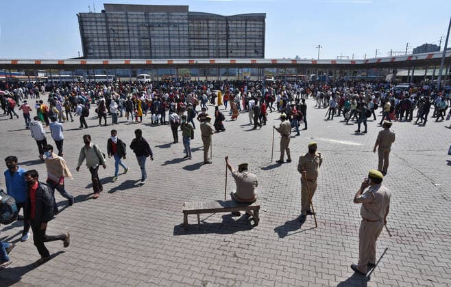NEW DELHI, INDIA - MARCH 28: Police personnel stand guard as migrant workers gather in large numbers at Kaushambi Roadways Bus Stand on Day 4 of the 21 day nationwide lockdown -- to check the spread of coronavirus, at Kaushambi, on March 28, 2020 in New Delhi, India. (Photo by Ajay Aggarwal Hindustan Times ) Coronavirus Update: Amid Lockdown, A Sea Of Migrants In Delhi-NCR Try To Find Their Way Back Home