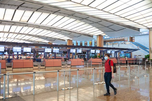 28.03.2020, Singapur, Republik Singapur, Asien - Ein Mann geht an geschlossenen Abflugschaltern in der leeren Abflughalle des Terminal 2 am Flughafen Changi vorbei und traegt dabei eine Atemschutzmaske, um sich vor einer Ansteckung mit dem pandemischen Coronavirus zu schuetzen. Durch die globale Verbreitung des Virus hat sich das weltweite Flugaufkommen drastisch reduziert und es kommt zu erheblichen Flugausfaellen.