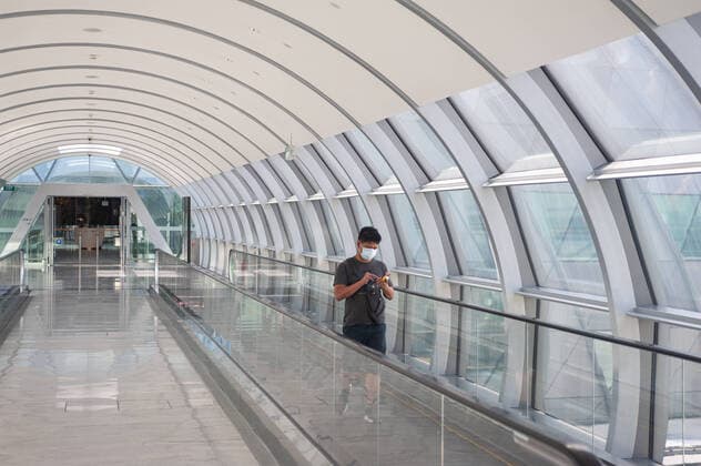 28.03.2020, Singapur, Republik Singapur, Asien - Ein Mann geht auf der Verbindungsbruecke zwischen Jewel Terminal and Terminal 2 am Flughafen Changi entlang und traegt dabei eine Atemschutzmaske, um sich vor einer Ansteckung mit dem pandemischen Coronavirus zu schuetzen.