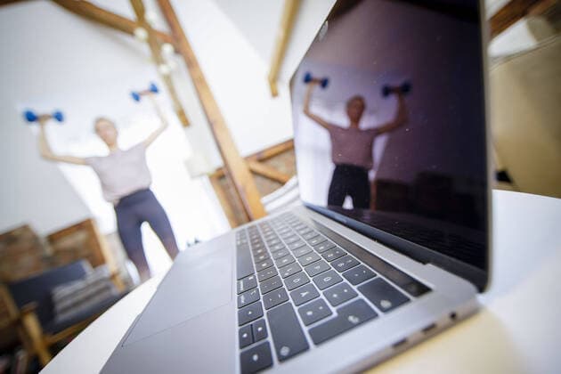 Symbolfoto zum Thema Fitness: Eine Frau trainiert zu Hause mit Hanteln. Neben ihr steht ein Laptop. Berlin, 26.03.2020. Berlin Deutschland