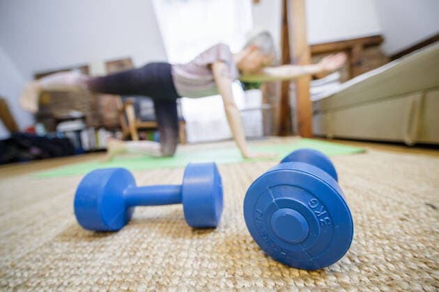 Symbolfoto zum Thema Fitness: Eine Frau trainiert zu Hause im Wohnzimmer. Vor ihr liegen zwei Hanteln. Berlin, 26.03.2020. Berlin Deutschland