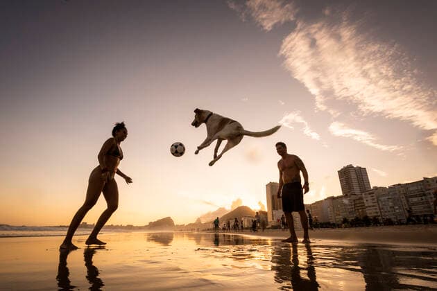 IMAGO Creative: Sommer Sport - Strand Couple playing soccer with dog on the water front in Copacabana Beach Rio de Janeiro, RJ, Brazil ,editorial use only CR_GNUJ200326C-328399-01