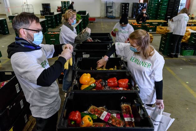 In einer Halle des Berliner Großmarkts packen ehrenamtliche Helfer der Berliner Tafel mit Atemschutzmasken Atemschutzmaske Lebensmittel in Tüten. Wegen der COVID-19-Pandemie mussten die 42 LAIB und SEELE -Ausgabestellen schließen. Damit bedürftige Menschen weiterhin gespendete Lebensmittel erhalten können, beliefert die Berliner Tafel die Bedürftigen jetzt zu Hause. snapshot-photography F.Boillot