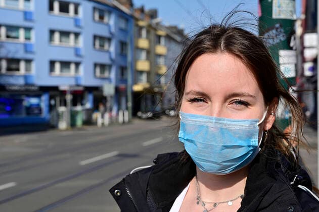 27.03.20, Essen, Nordrhein-Westfalen, Deutschland. . Zum Schutz vor Ansteckung mit dem Corona Virus hat das Land NRW verschaerfte Sicherheitsmassnahmen zur Ausbreitung des Virus verhaengt. Es gilt ein generelles Kontaktverbot. Nur noch maximal 2 Personen duerfen sich zusammen im Freien bewegen. Desweiteren gilt es einen Sicherheitsabstand von 1,5 bis 2 Metern zu anderen Menschen zu wahren. Junge Frau mit Mundschutz im Essener-Suedviertel. Alltagsleben waehrend der Corona Krise