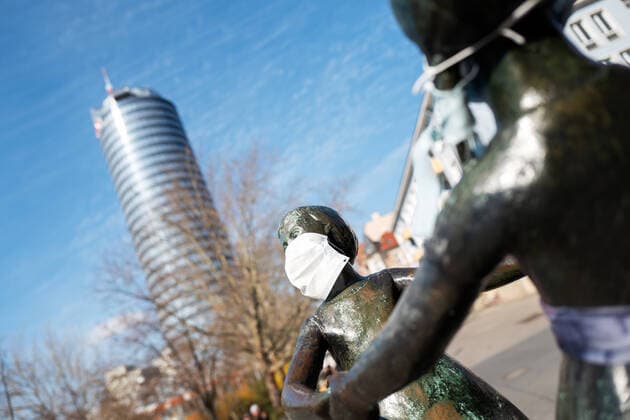 Die Statue der beiden tanzenden Mädchen im Zentrum von Jena, die Unbekannte mit Atemmasken versehen haben. Im Hintergund der JenTower. Foto vom 2.4.2020. Innenstadt Jena