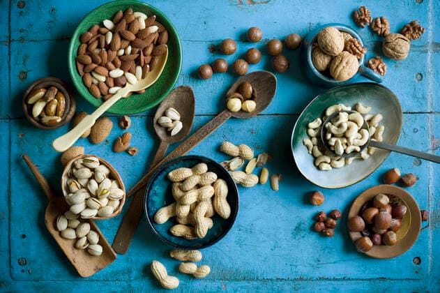 Overhead view of various nuts in bowls and on spoons on blue rustic table  ASF06581