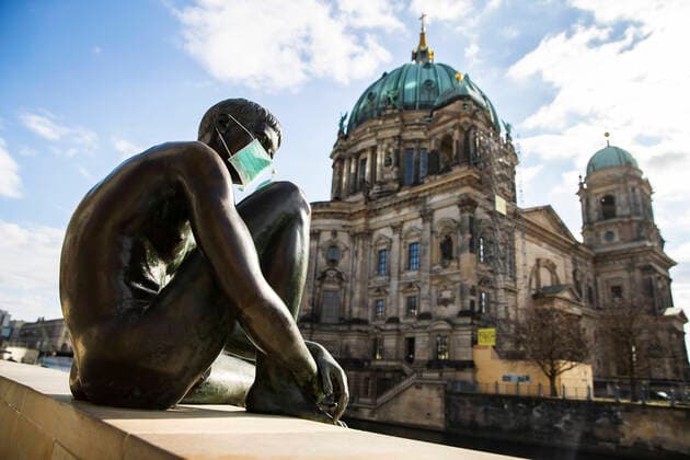 Gestelltes Bild: Statue mit Mundschutzmaske am Spreeufer in Berlin am 2. April 2020. Um die Verbreitung des Coronavirus (SARS-CoV-2) zu verlangsamen beschlossen Bund und Laender weitere Restriktionen. Nachdem Museen, Theatern, Sportveranstaltungen usw verboten wurden sind seit einigen Tagen weitere verschaerfte Massnahmen in Kraft getreten wie z.B. Verbot von Versammlungen in der Oeffentlichkeit mit mehr als zwei Personen, Einhaltung von Mindestabstand zwischen Personen und Schliessung von Gastronomiebetrieben mit Ausnahme von Abholung und Lieferung. Coronavirus in Berlin