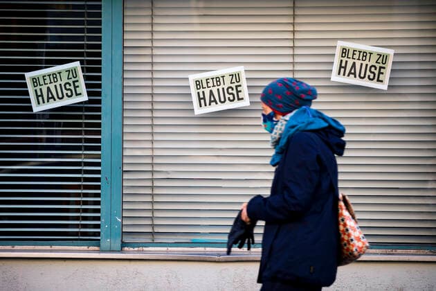 Eine Frau mit Mundschutzmaske laeuft vor Schilder Bleib zu Hause in Berlin am 2. April 2020. Um die Verbreitung des Coronavirus (SARS-CoV-2) zu verlangsamen beschlossen Bund und Laender weitere Restriktionen. Nachdem Museen, Theatern, Sportveranstaltungen usw verboten wurden sind seit einigen Tagen weitere verschaerfte Massnahmen in Kraft getreten wie z.B. Verbot von Versammlungen in der Oeffentlichkeit mit mehr als zwei Personen, Einhaltung von Mindestabstand zwischen Personen und Schliessung von Gastronomiebetrieben mit Ausnahme von Abholung und Lieferung. Coronavirus in Berlin