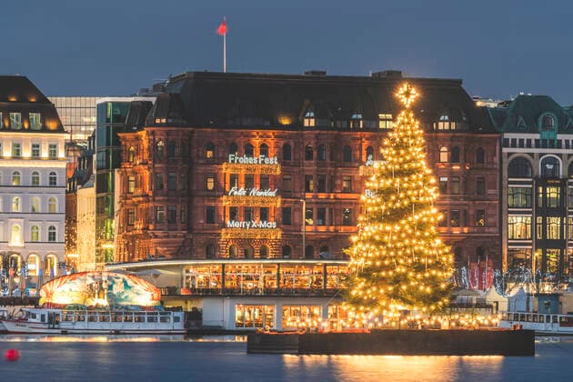 Germany, Hamburg, Illuminated Alstertanne tree at dusk with Jungfernstieg promenade in background  KEBF01486
