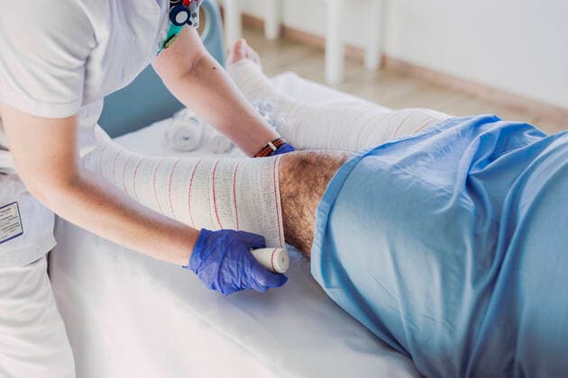 Nurse wrapping bandage around patient s leg in hospital bed model released Symbolfoto property released  LJF01353