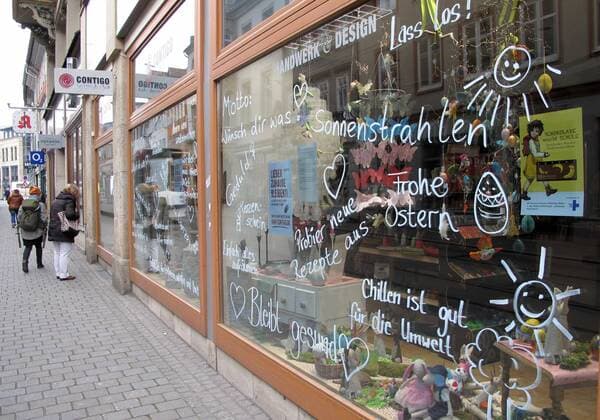 Corona 03.04.2020 , Erfurt, die Innenstadt ist aufgrund der Verordnungen wegen Corona wie ausgestorben, an einem Geschäft in der Schlösserstrasse wurden viele Botschaften aufgemalt, u.a. Bleibt gesund, Frohe Oster, Grillen ist gut für die Umwelt, Sonnenstrahlen, Probier neue Rezepte aus, im Hintergrund sind ein paar Passanten unterwegs