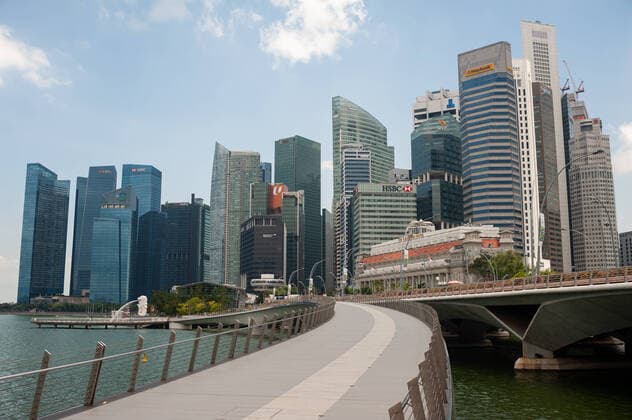 02.04.2020, Singapur, Republik Singapur, Asien - Blick auf die Skyline mit Wolkenkratzern im Geschaeftsviertel und der Jubilee Bridge entlang des Ufers in Marina Bay. Seit dem Ausbruch der Corona-Pandemie ist die Zahl auslaendischer Besucher komplett zurueck gegangen. Fuer gewoehnlich wimmelt die Gegend um Marina Bay von Touristen, ist jetzt aber bis auf wenige Personen total verwaist.