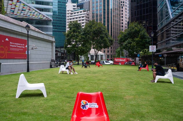 02.04.2020, Singapur, Republik Singapur, Asien - Menschen sitzen im Geschaeftsviertel am Raffles Place raeumlich voneinander getrennt auf Plastikstuehlen, um eine Ansteckung mit dem pandemischen Coronavirus zu verhindern. Um die Ausbreitung des Coronavirus weiter einzuschraenken sind Massnahmen zur Einhaltung von Sicherheitsabstaenden (Safe Distancing) im oeffentlichen Leben eingefuehrt worden, was zur raeumlichen Distanzierung (Social Distancing) fuehrt und somit den unmittelbaren Kontakt mit Mitmenschen verhindern soll.