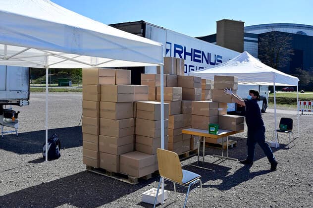 04.04.20, Oberhausen, Nordrhein-Westfalen, Deutschland. Corona Krise. Auf dem Gelaende eines Parkplatzes am Centro Oberhausen wird Schutzmaterial fuer Aerzte von der Kassenaerztlichen Vereinigung Niederrhein kostenlos verteilt. Mittels eines zugestellten QR-Codes koennen die Aerzte ihre Kartons an der Ausgabestelle abholen. Zwei LKW-Ladungen mit Kartons stehen bereit. In jedem KArton befinden sich Desinfektionsmittel und Mundschutzmasken, die aus China impotiert wurden. Blick auf die Ausgabestelle der Pakete. Alltagsleben waehrend der Corona Krise