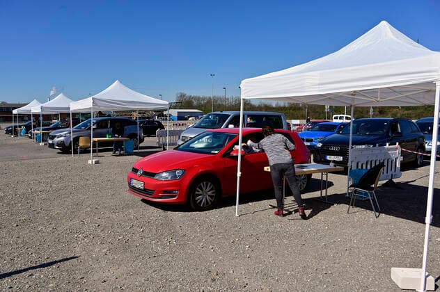 04.04.20, Oberhausen, Nordrhein-Westfalen, Deutschland. Corona Krise. Auf dem Gelaende eines Parkplatzes am Centro Oberhausen wird Schutzmaterial fuer Aerzte von der Kassenaerztlichen Vereinigung Niederrhein kostenlos verteilt. Mittels eines zugestellten QR-Codes koennen die Aerzte ihre Kartons an der Ausgabestelle abholen. Zwei LKW-Ladungen mit Kartons stehen bereit. In jedem KArton befinden sich Desinfektionsmittel und Mundschutzmasken, die aus China impotiert wurden. Ehrenamtliche Helferin ueberprueft an der Einfahrt zur Ausgabestelle die jeweiligen QR-Codes auf dem Anschreiben, die den Aerzten zugestellt wurden. Alltagsleben waehrend der Corona Krise