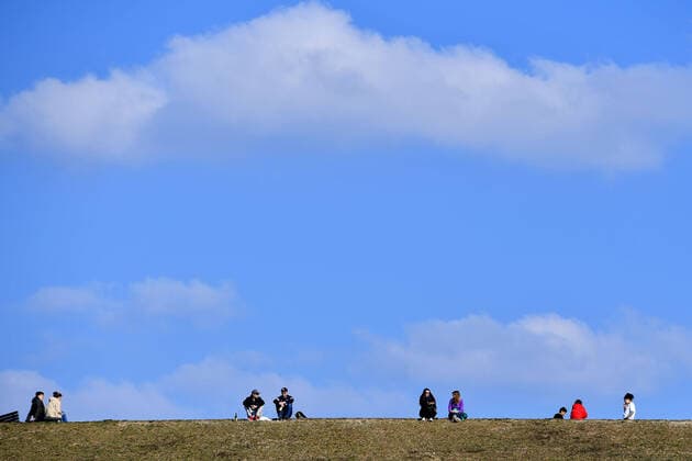 Oeffentliches Leben in Zeiten der Corona Pandemie am 04.04.2020 im Riemer Park in Muenchen. Familien,Menschen,Personen sitzen im Gras auf einem Huegel vor blauem Himmel. Das fruehlingshafte Wetter treibt die Bevoelkerung an die frische Luft,immer mit dem noetigen Abstand wegen einer Ansteckung mit dem Coronavirus. Ausgangsbeschraenkungen,Kontaktsperre.