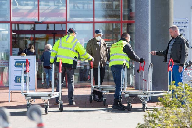 04.04.2020, xtgx, Auswirkungen des Corona Virus in Wolfsburg, Mitarbeiter des Sicherheitsdienstes kontrollieren desinfizieren Einkaufswagen am Eingang des Bau King (Hagebaumarkt, Hagebau, Baumarkt) in Vorsfelde (Wolfsburg). In Niedersachsen duerfen seit diesem Samstag die Baumaerkte wieder fuer Privatpersonen oeffnen, allerdings darf nur eine bestimmte Zahl von Kunden mit Einkaufswagen in den Markt. Wolfsburg