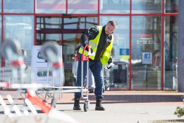 04.04.2020, xtgx, Auswirkungen des Corona Virus in Wolfsburg, Mitarbeiter des Sicherheitsdienstes kontrollieren desinfizieren Einkaufswagen am Eingang des Bau King (Hagebaumarkt, Hagebau, Baumarkt) in Vorsfelde (Wolfsburg). In Niedersachsen duerfen seit diesem Samstag die Baumaerkte wieder fuer Privatpersonen oeffnen, allerdings darf nur eine bestimmte Zahl von Kunden mit Einkaufswagen in den Markt. Wolfsburg