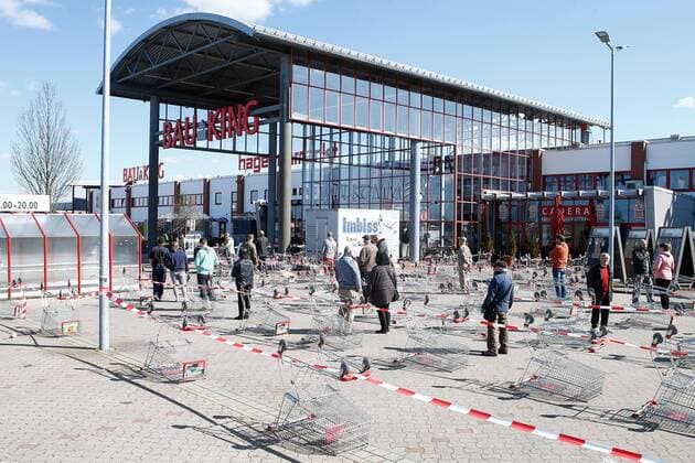 04.04.2020, xtgx, Auswirkungen des Corona Virus in Wolfsburg, Kunden warten in einer langen Schlagen, um einzeln den Bau King (Hagebaumarkt, Hagebau, Baumarkt) in Vorsfelde (Wolfsburg) betreten zu duerfen. In Niedersachsen duerfen seit diesem Samstag die Baumaerkte wieder fuer Privatpersonen oeffnen, allerdings darf nur eine bestimmte Zahl von Kunden mit Einkaufswagen in den Markt. Aus umgedrehten Einkaufswagen und Absperrband wurde ein Wartebereich wie am Flughafen gestaltet, in dem die Menschen in einer Warteschlange im Zickzack warten. Wolfsburg