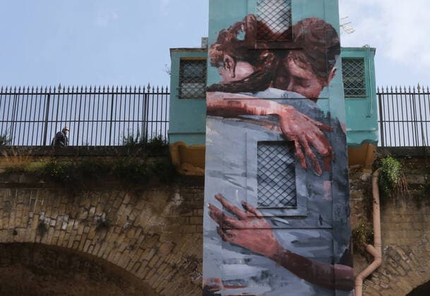 A man walks on Sanit ¡ bridge next to a mural painting depicting a hug wearing a protective mask. In Italy the lockdown still continue Government Decree declaring all of Italy a protected area to combat covid-19 - coronavirus infection, closing schools, public offices and shops.  Copyright: xCarloxHermannx xIPAx xKontrolabx