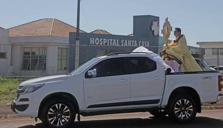 Coronavirus in Brasilien, motorisierte Prozession zum Beginn der Karwoche in Campo Mourao CAMPO MOURÃO, PR - 05.04.2020: COVID 19 ESPANTA FIES NO DOMINGO DE RAMOS - Catholics in Campo Mourão, in the Midwest Region of Paraná, celebrated Palm Sunday? beginning of Holy Week? from the gate into the residences. The faithful placed a green branch on the gates of the houses waiting for the passage of the Most Holy. Due to the recommendation of social isolation due to the Covid-19 pandemic, a disease caused by the coronavirus, a priest held a small procession blessing the homes and people of neighborhoods close to the city center. In the photo, a priest visits the sick at Santa Casa de Campo Mourão. x1901691x  DirceuxPortugal