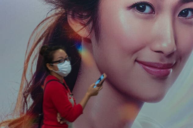02.04.2020, Singapur, Republik Singapur, Asien - Eine Frau geht in einer Fussgaengerunterfuehrung an einer Werbeflaeche vorbei und traegt dabei eine Atemschutzmaske, um sich vor einer Ansteckung mit dem pandemischen Coronavirus zu schuetzen.