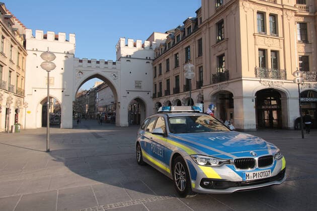 Streifenwagen der Landespolizei Bayern stehen während einer Kontrolle anlässlich der Coronakrise über die Einhaltung der Kontaktverbote sowie Mindestabstände am ansonsten von Passanten stark frequentierten Karlsplatz Stachus vor dem Karlstor in der Innenstadt von München, Bayern, Deutschland