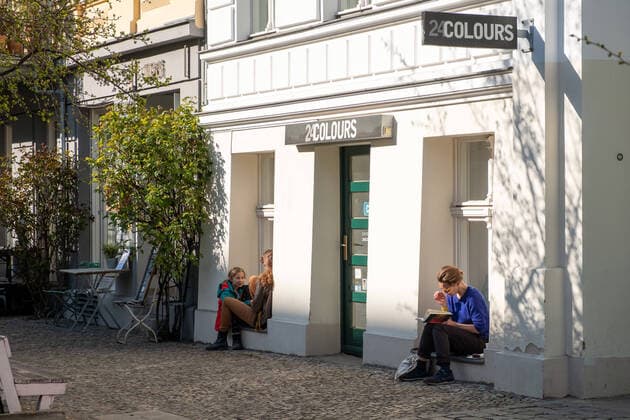 Menschen genießen das warme und sonnige Frühlingswetter mit genügend Abstand zueinander auf den Fensterbänken geschlossener Läden und Cafés Prenzlauer Berg auf der Oderberger Strasse. Coronakrise - Frühlingswetter mit dem Virus