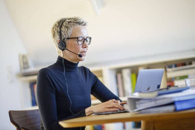 Symbolfoto zum Thema Homeoffice. Eine Frau sitzt zu Hause am Schreibtisch. Sie traegt ein Headset und nimmt an einer Videokonferenz teil. Berlin, 06.04.2020. Waehrend der Ausgangssperre und Quarantaene aufgrund des Coronavirus, COVID-19, SARS-CoV-2 sind viele Arbeitnehmer gezwungen, von zu Hause aus zu arbeiten. Berlin Deutschland