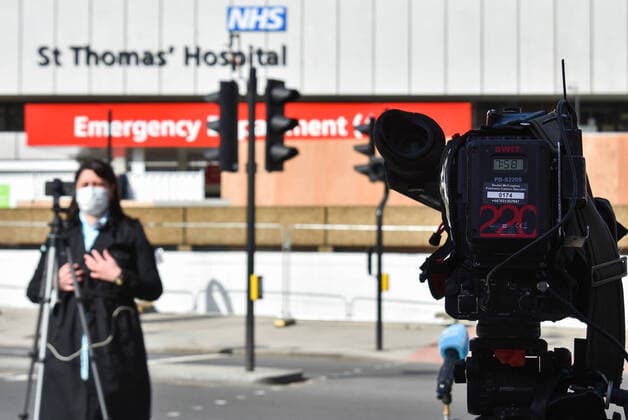 LONDON, UNITED KINGDOM - APRIL 7, 2020: A reporter in a face mask broadcasts an update over the internet from outside St Thomas Hospital where British Prime Minister Boris Johnson is being treated for the novel coronavirus (COVID-19) infection. The prime minister was admitted to the hospital on 5 April and taken to intensive care on the next day. Seen in the distance is Victoria Tower of the Houses of Parliament (Westminster Palace). Ilya Dmitryachev TASS  TS0D4C05