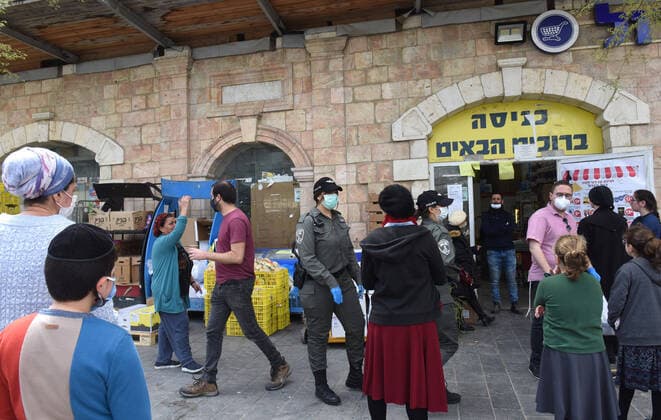 Israeli border police patrol between people waiting to enter a supermarket, because of coronavirus restrictions, before the Jewish holiday of Passover, on Tuesday, March 7, in Jerusalem. Israeli Prime Minister Benjamin announced severe travel restrictions and a curfew for the Passover holiday, as an effort to halt the spread of the coronavirus.  JER2020040702 DEBBIExHILL