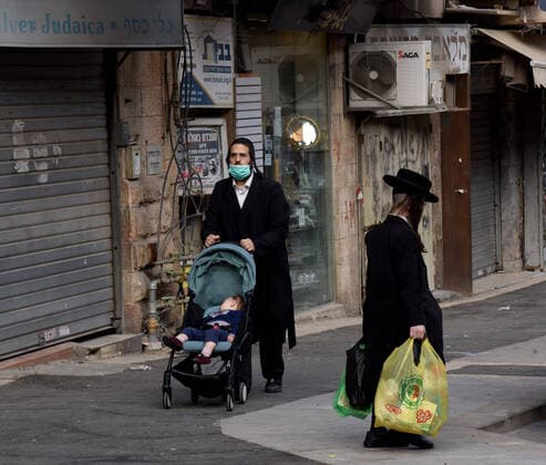 An Ultra-Orthodox Jew wears a mask, as protection from the coronavirus, while pushing a baby carriage, on Tuesday, March 7, in Mea Shearim in Jerusalem. Israeli Prime Minister Benjamin announced severe travel restrictions and a curfew for the Passover holiday, as an effort to halt the spread of the coronavirus.  JER2020040715 DEBBIExHILL