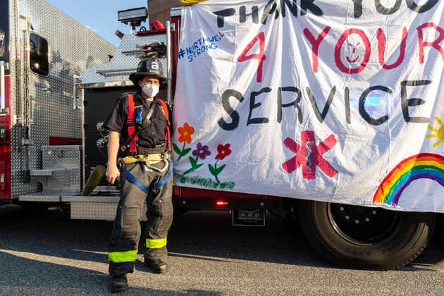 NY: Nassau County first responders salute medics Firefighter Brett Auerbach poses next to poster created by his kids during Nassau County first responders line up to salute heroes from front lines of COVID-19 pandemic at North Shore University Hospital Manhasset New York United States Copyright: LevxRadin