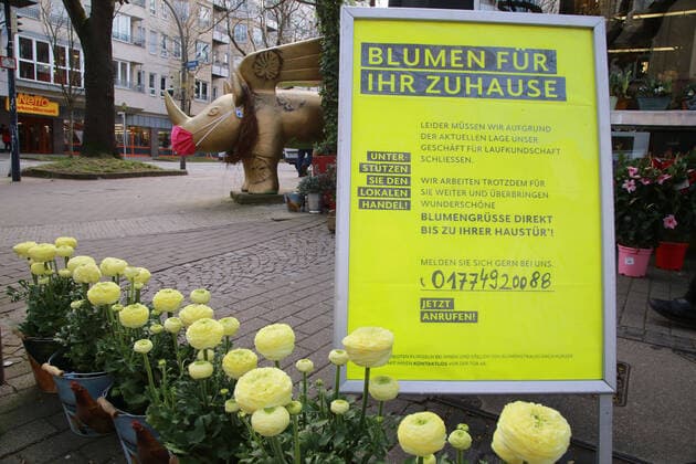 07.04.2020 Dortmund Die Coronakrise verschärft sich. Die Bundes- und Landesregierungen erlassen umfasssenden Richtlinien. In allen Lebensbereichen erleben auch die Dortmunder Bürger starke Einschränkungen.. Für Blumengrüße für zuhause wirbt ein Blumengeschäft auf einem Aufsteller vor dem Laden. Im Hintergrund ist ein Dortmund-Rhino mit Schutzmaske zu sehen. Das geflügelte Nashorn ist das Wappentier des Dortmunder Konzerthauses und konnte in Speziallackierung von Geschäftsleuten und interessierten Bürgern erworben werden. Dieses steht seit längerer Zeit vor dem Geschäft und wird passend zur Jahreszeit dekoriert.