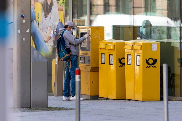 DEU, Deutschland, Baden-Württemberg, Stuttgart, 09.04.2020: Alltag in Zeiten von Corona. Ein Mann mit Mundschutz und Schutzhandschuhen an einem Briefmarkenautomat der Deutschen Post.