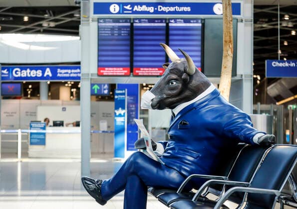 09.04.2020, Duesseldorf, Nordrhein-Westfalen, Deutschland - Flughafen Duesseldorf, menschenleere Abflughalle in Zeiten der Coronakrise, einer Bullen-Werbefigur wurde ein Mundschutz angeklebt, ein bullischer Boersianer mit Mundschutz liest das Handelsblatt. Duesseldorf Nordrhein-Westfalen Deutschland