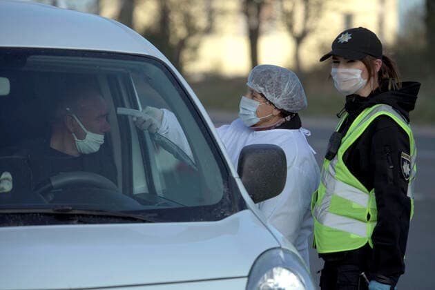 ZOLOCHIV, UKRAINE - APRIL 10, 2020 - A healthcare worker accompanied by a police officer measures the body temperature of a driver at a roadblock set up on the border with Ternopil Region during the COVID-19 outbreak, Zolochiv, Lviv Region, western Ukraine. Roadblock in Zolochiv  Copyright: xMARKIIANxLYSEIKOx